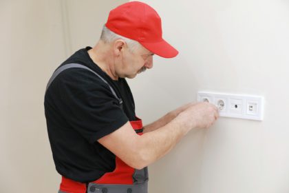 Electrician hands tighten electrical wires in wall fixture or socket using a screw driver - closeup