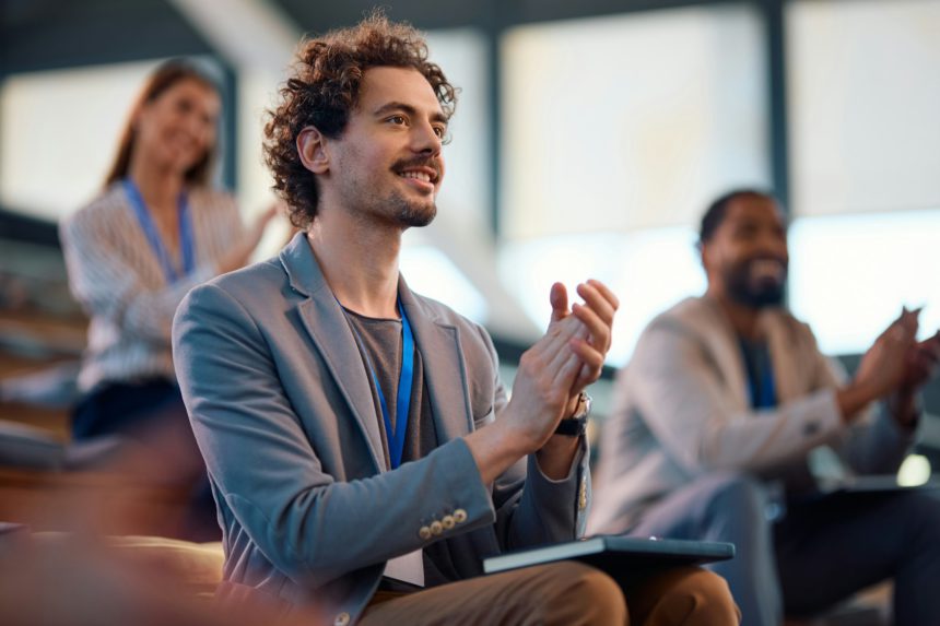 Happy entrepreneur applauding after successful business seminar in conference hall.